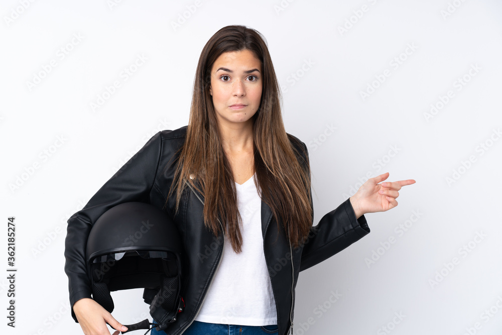 Young woman with a motorcycle helmet over isolated white background pointing to the laterals having doubts Young woman with a motorcycle helmet over isolated white background pointing to the laterals having doubts