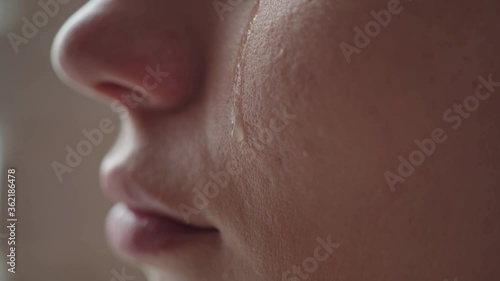 Close-up of a woman's cheek with a tear sliding down it. A tear slowly descends on the distressed face of a young girl, macro photo