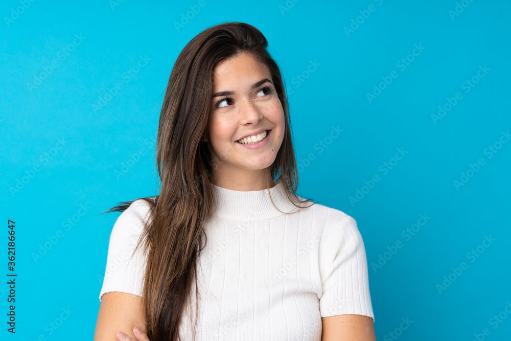 Teenager girl over isolated blue background looking up while smiling Teenager girl over isolated blue background looking up while smiling