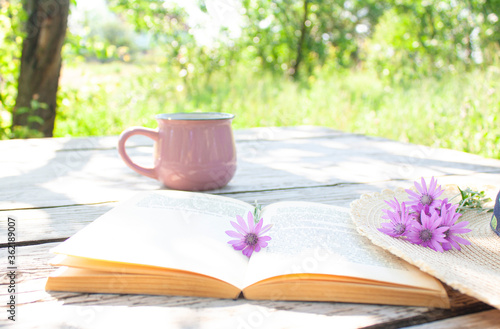 open book, cup, hat and wildflowers in bloom on a wooden table in the garden