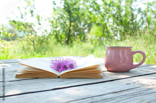 open book with a bouquet of wildflowers on its pages and a cup on a table in the garden