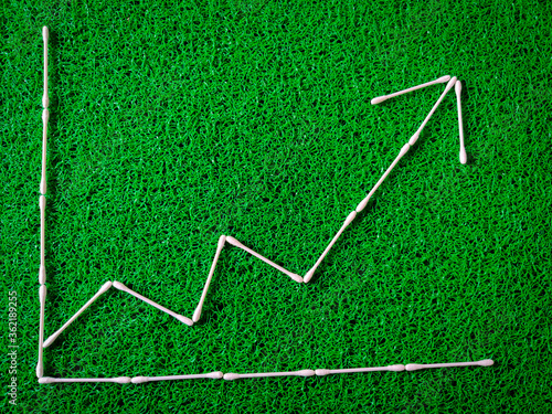 Cotton ear sticks arranged as a Increase and decrease graph on green background. Business concept