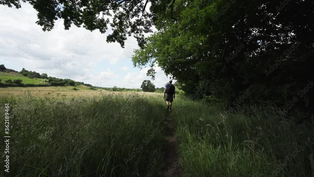 A man walking along a path through long grass in England A man walking along a path through long grass in England