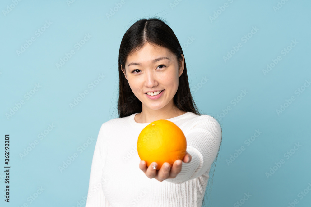 Young asian woman holding an orange over isolated blue background Young asian woman holding an orange over isolated blue background