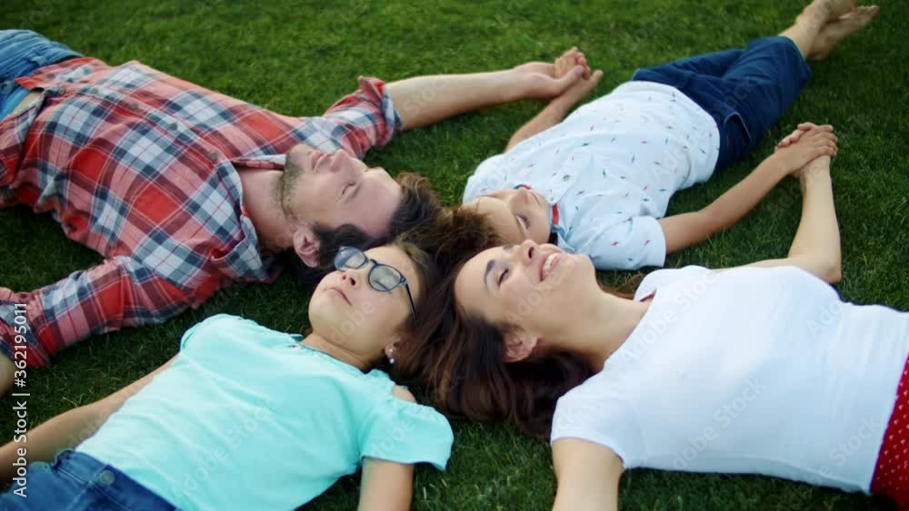 Family lying in circle on grass outdoors. Parents and children holding hands Family lying in circle on grass outdoors. Parents and children holding hands