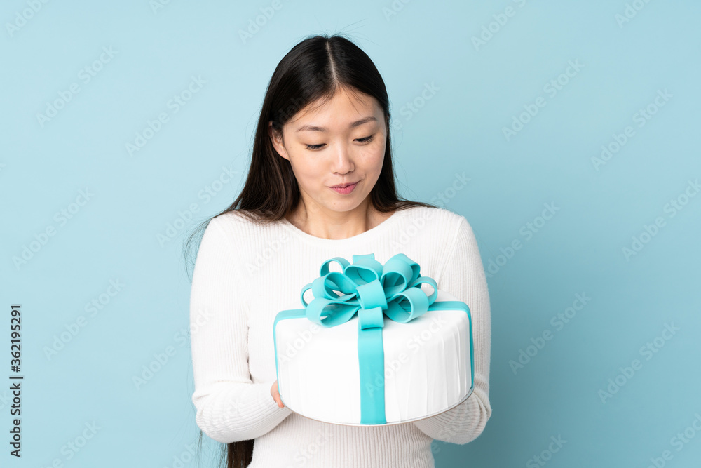 Pastry asian chef holding a big cake isolated on blue background Pastry asian chef holding a big cake isolated on blue background