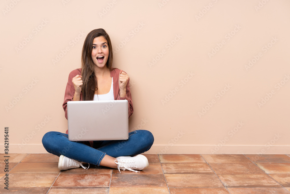 Teenager student girl sitting on the floor with a laptop celebrating a victory in winner position Teenager student girl sitting on the floor with a laptop celebrating a victory in winner position
