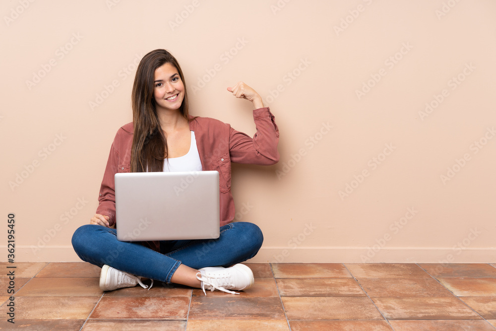 Teenager student girl sitting on the floor with a laptop doing strong gesture Teenager student girl sitting on the floor with a laptop doing strong gesture