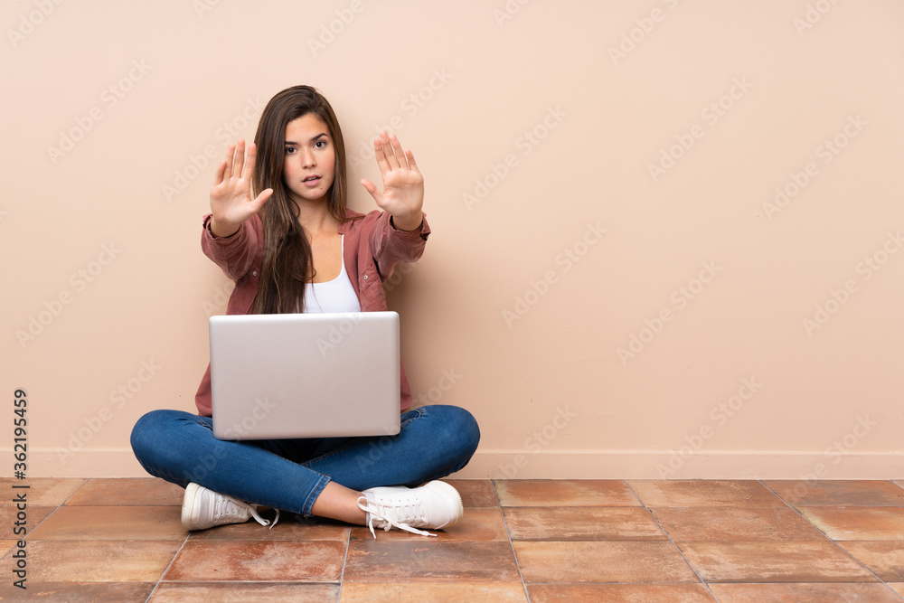 Teenager student girl sitting on the floor with a laptop making stop gesture and disappointed Teenager student girl sitting on the floor with a laptop making stop gesture and disappointed