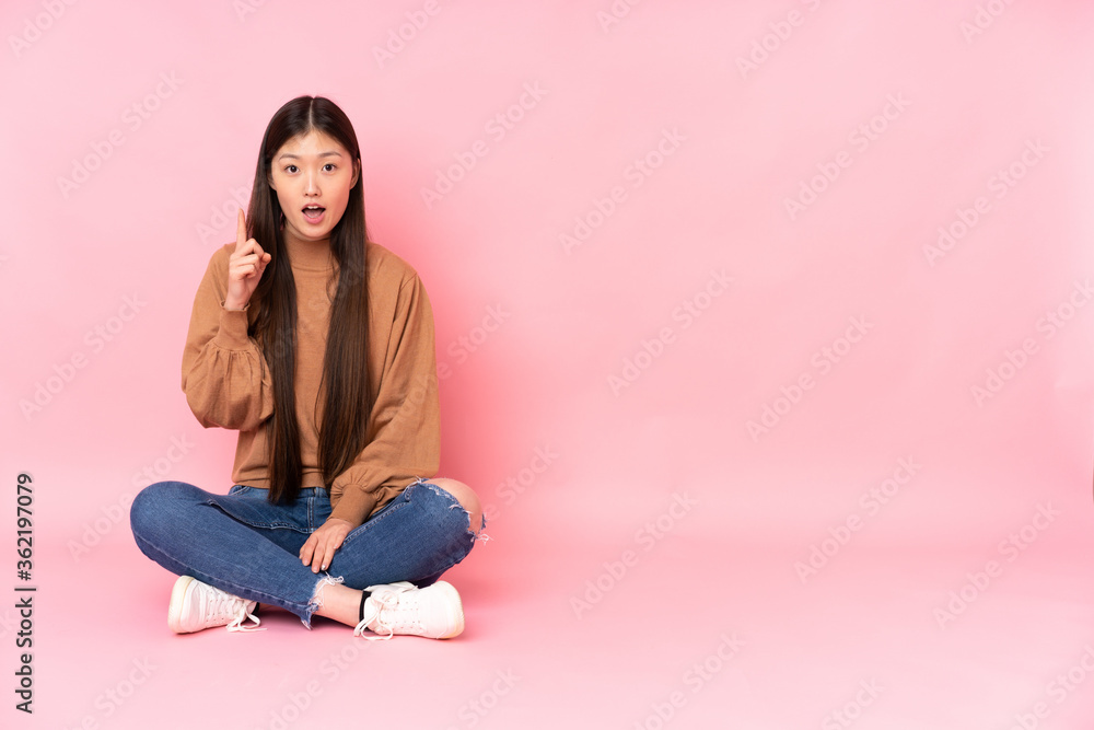 Young asian woman sitting on the floor isolated on pink background thinking an idea pointing the finger up Young asian woman sitting on the floor isolated on pink background thinking an idea pointing the finger up