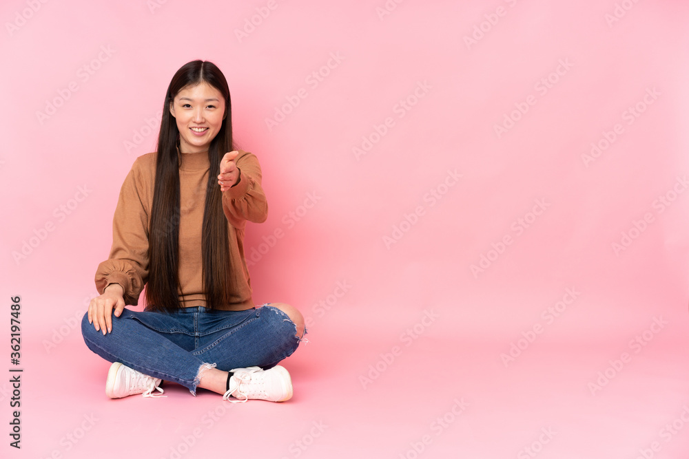 Young asian woman sitting on the floor isolated on pink background shaking hands for closing a good deal Young asian woman sitting on the floor isolated on pink background shaking hands for closing a good deal