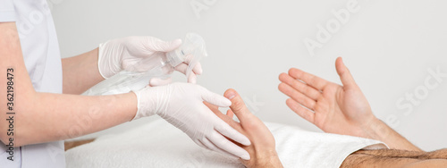 Nurse hand sanitizing hands of male patient in the hospital. Coronavirus protection concept.