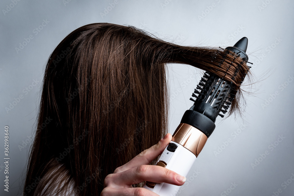 Fototapeta premium Young woman with a hairdryer and comb brushing her hair.