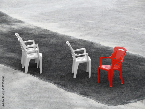 Three white chairs and one red on dark asphalt