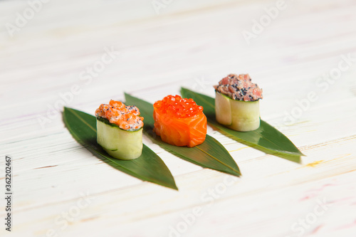 Set of Japanese Gunkan Maki Sushi Rolls: Sake with salmon caviar, tuna Maguro and salmon in cucumber served on bamboo leaves. Pan Asian dish on wooden board. Expensive seafood restaurant meal close up