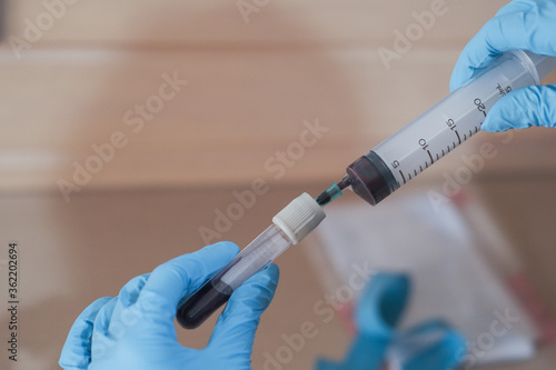 Nurse Hand with blue glove holding syringe and green needle on laboratory blood tube