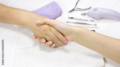Women manicurist and client shake hands in the salon for the care of hands and nails. A woman greets a customer. Beauty salon. Thank you for a job well done. Close-up handshake  pink manicure.