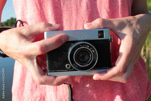 Close-up of old camera in hands. Young woman in pink t-shirt holding vintage film camera. 