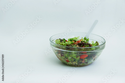 fresh vegetable salad tomatoes, cucumbers, lettuce leaves, pine nuts, walnuts and seeds in a transparent large plate with a white spoon on a white background