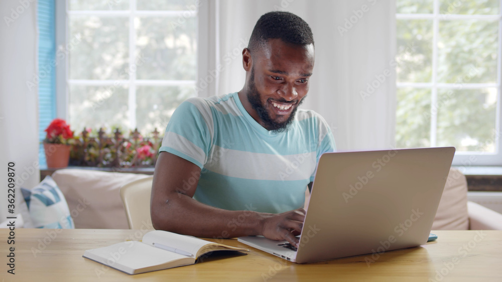 Cheerful afro guy working on laptop from home office Cheerful afro guy working on laptop from home office