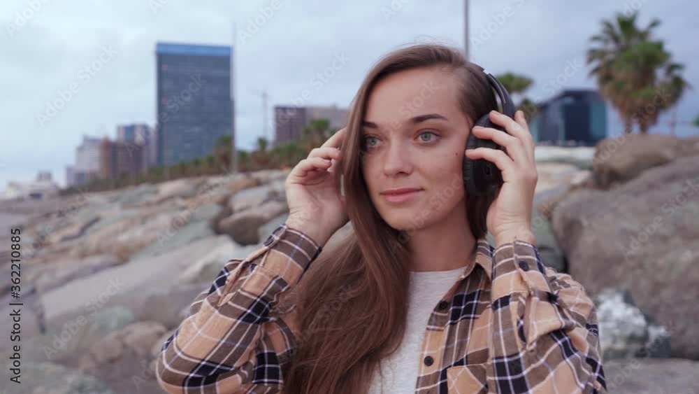 Young casual woman puts on black wireless headphones and listens to music outdoors Young casual woman puts on black wireless headphones and listens to music outdoors