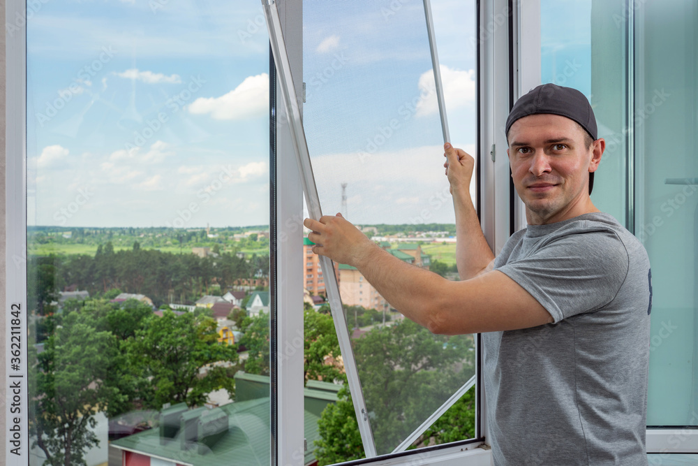 A contractor worker installing mosquito wire screen on house plastic windows to protect from insects. A contractor worker installing mosquito wire screen on house plastic windows to protect from insects.