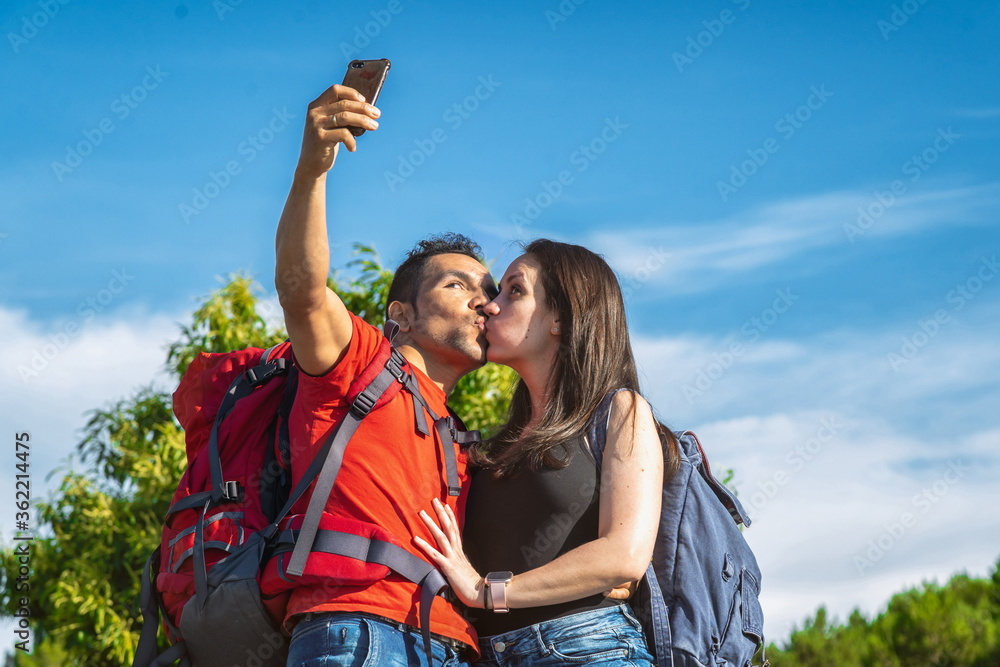 Naklejka premium Couple of hikers in the mountains kissing taking a photo with the mobile
