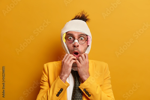 Emotional frightened man bites finger nails and stares with fright, has bruised hurt face after fight and assault, becomes victim of family violence, afraids of offender, wears formal yellow suit