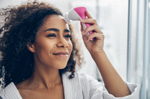 Photography Dreamy woman applying an electric facial cleansing brush