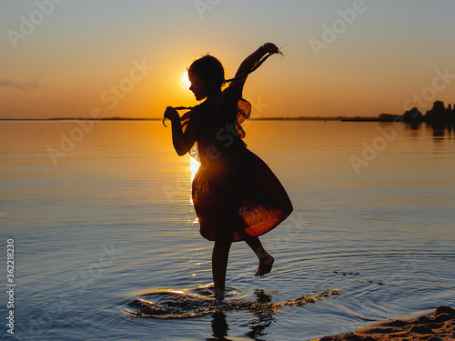 Silhouette of a dancing girl at sunset on the background of the river. Summer vacation concept.