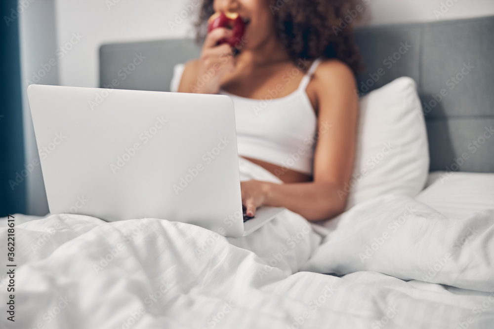 Curly-headed female eating an apple in bed Curly-headed female eating an apple in bed