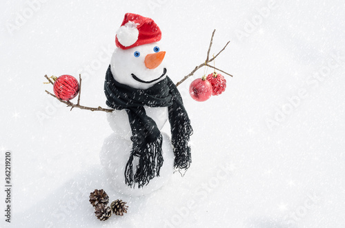 Christmas and New Year background greeting card with copy space. Snowman in Santa's red hat and scarf on the snow with Christmas balls. Winter © Victoria