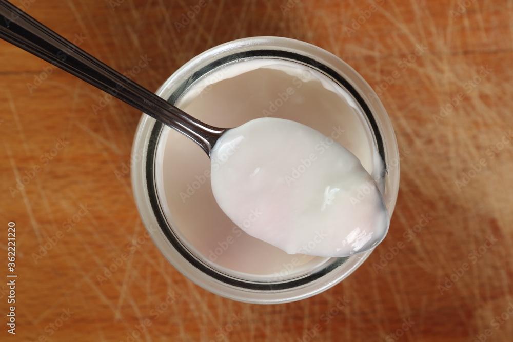 Spoon with yogurt on open small glass jar on wooden cutting boar Spoon with yogurt on open small glass jar on wooden cutting boar