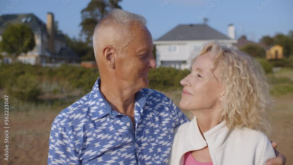 Happy senior couple hugging on sandy beach over country house background Happy senior couple hugging on sandy beach over country house background