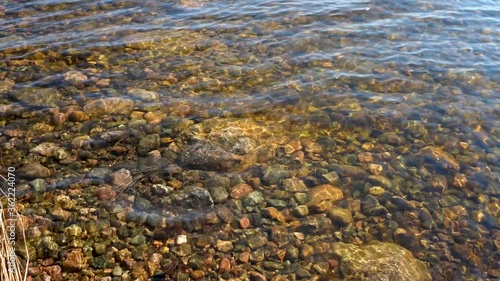Sun shining through water to stones visible through clear water at bottom of the lake Saimaa. Waves on the lake's surface.