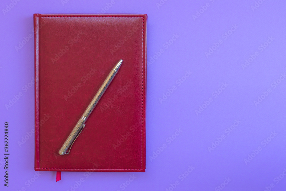Red leather notebook and silver pen on purple background. Business concept, top view, close-up, horizontal, text space, isolated Red leather notebook and silver pen on purple background. Business concept, top view, close-up, horizontal, text space, isolated
