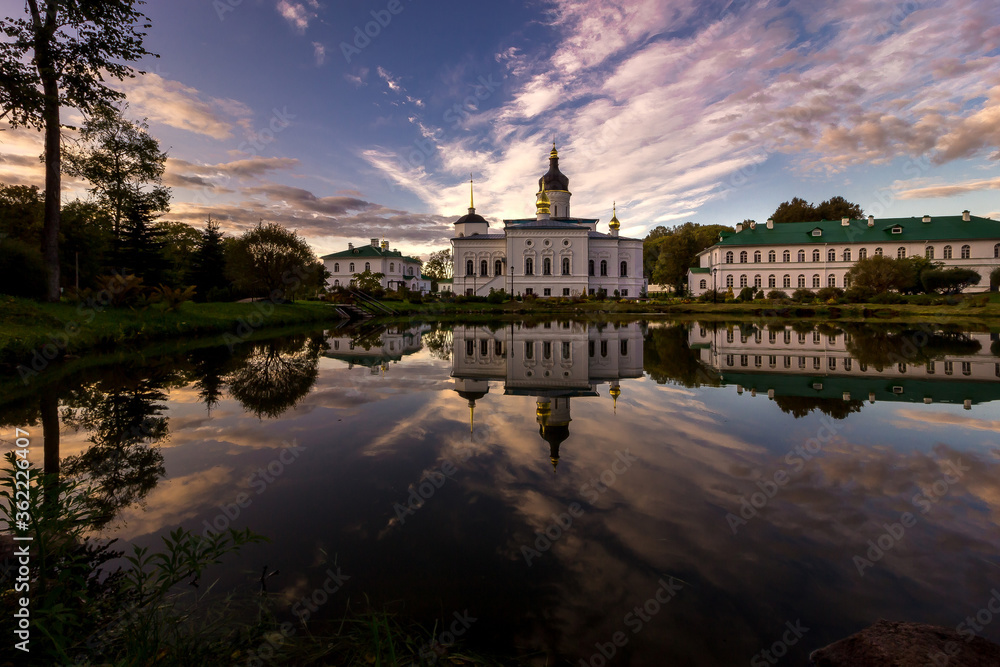 Panorama from a lower angle at the edge of the lake to an ancient white nunnery at sunset or sunrise with reflection of clouds in blue and lilac water
