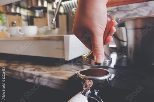 Barista pressing coffee grounds into a portafilter with a tamper.	