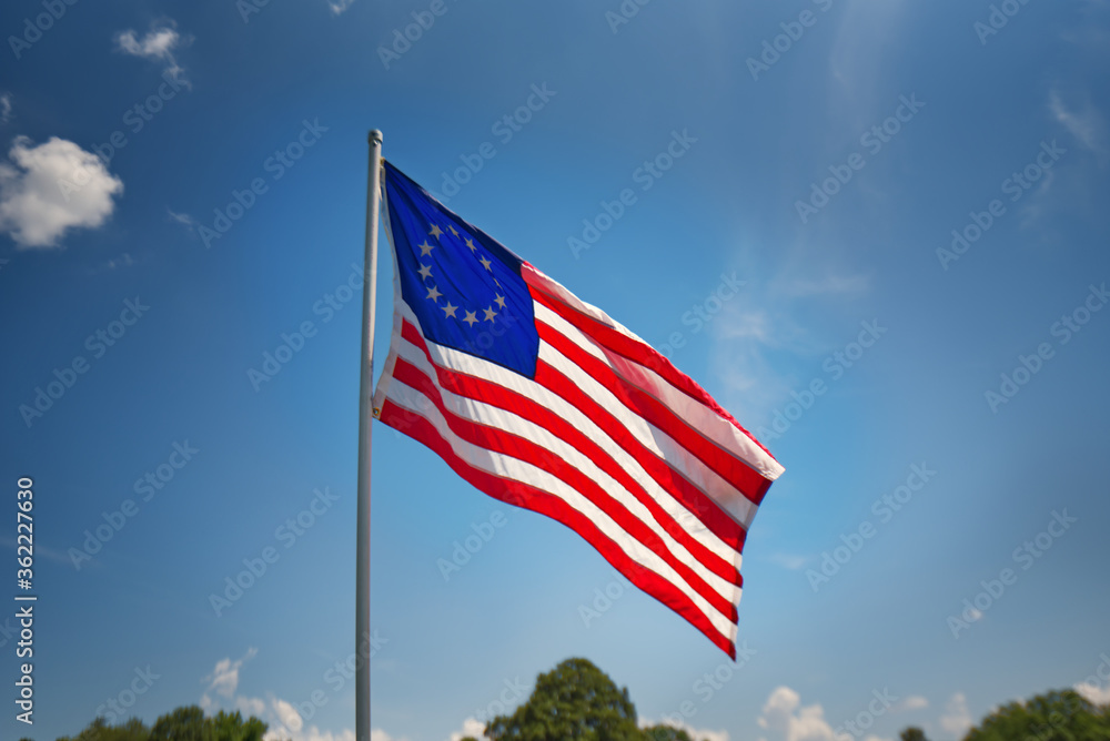A copy of the Betsy Ross American flag with 13 stars flying against a blue sky.