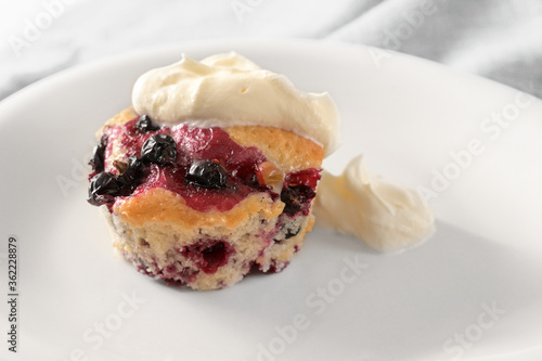 Homemade muffin with black currant berries and whipped cream on a white plate, fruity sweet dessert, copy space