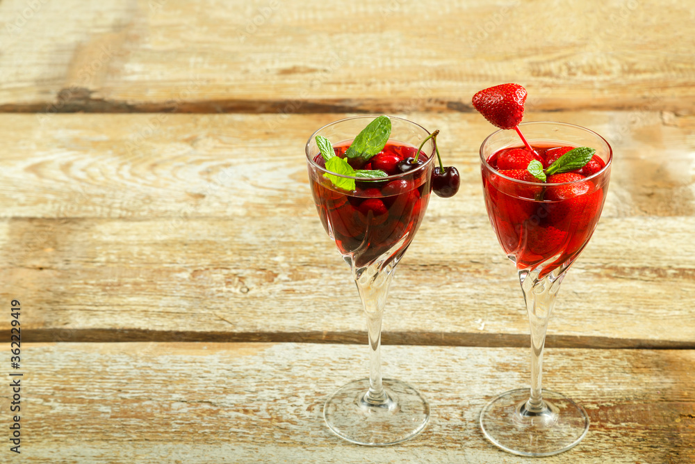 Crystal glass with cherry juice and strawberry and fresh berries and mint inside on a wooden table. Copy space. Crystal glass with cherry juice and strawberry and fresh berries and mint inside on a wooden table. Copy space.