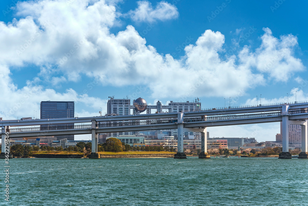 Fototapeta premium Seascape of the double-layered expressway of the suspension Rainbow Bridge with the shopping malls of Odaiba island whose the famous hachitama observatory sphere.