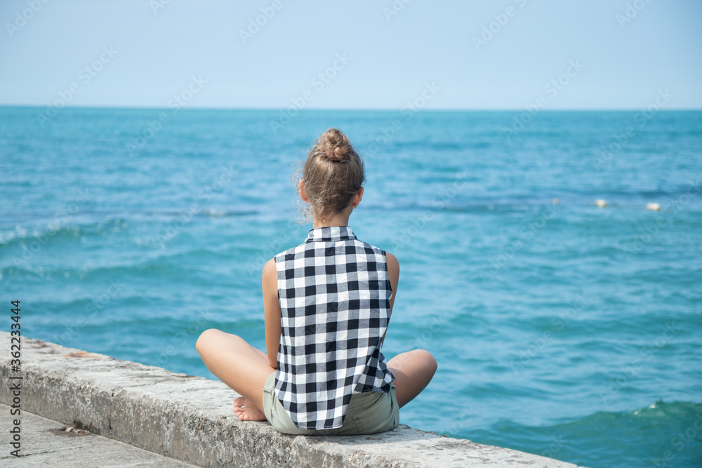 The girl is sitting facing the sea on the breakwater