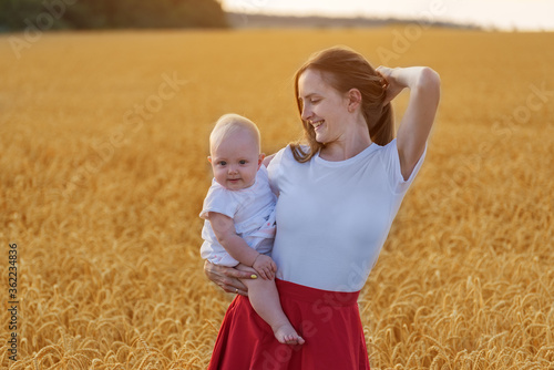 Beautiful young woman with child on background of yellow fields. Mother and child at sunset outdoors