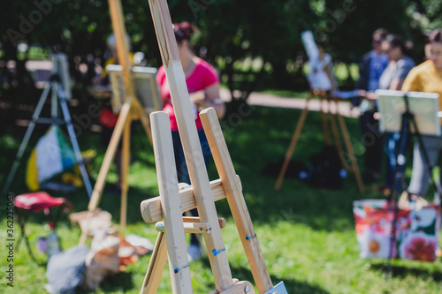 Fototapeta Naklejka Na Ścianę i Meble -  Process of plein air painting, group class of adult talented students in the park with paints easels, and canvases during lesson of watercolour painting outdoors
