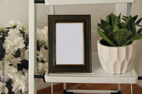 Blank wooden photo frame surrounded by home plants. Comfy details in the bedroom.