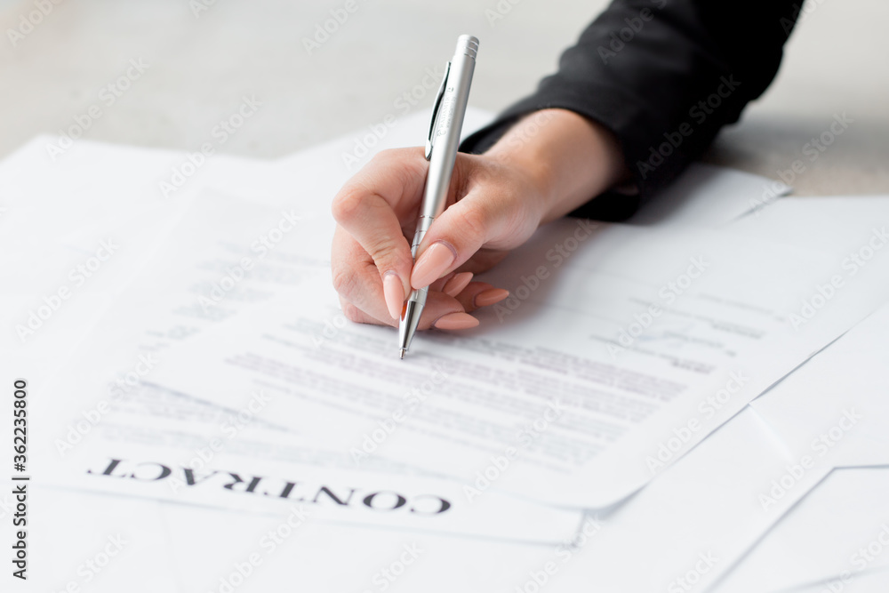 Woman's hand with pen signing document, close up Woman's hand with pen signing document, close up