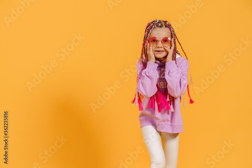 Stylish girl in rounded glasses with pink dreadlocks posing on a yellow background. Beauty, fashion.