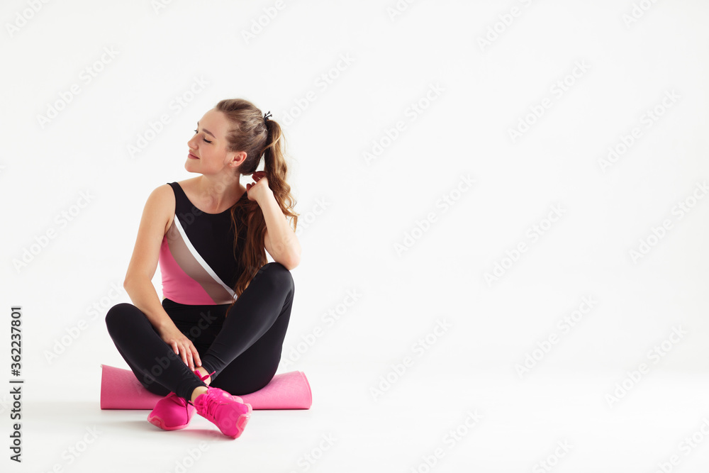 Fototapeta premium Smiling multiracial female yogi girl sit on rubber mat before yoga class, happy woman waiting for pilates training in white fitness studio. sport center banner for website header design.