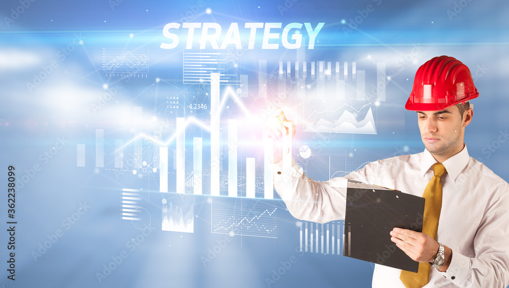 Handsome businessman with helmet drawing STRATEGY inscription, architecture business plan concept Handsome businessman with helmet drawing STRATEGY inscription, architecture business plan concept
